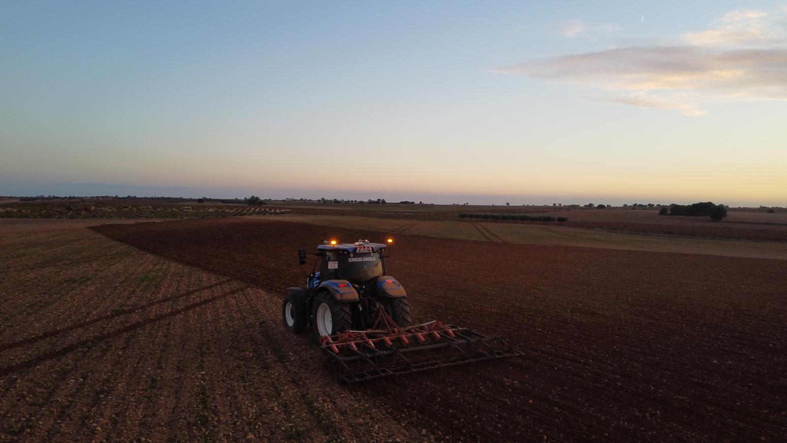 Tractor preparando la tierra con la grada al atardecer